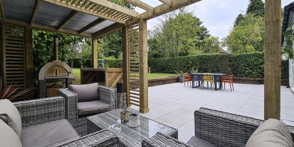 A grey porcelain patio seating area with a trellis roof and wood burning stove